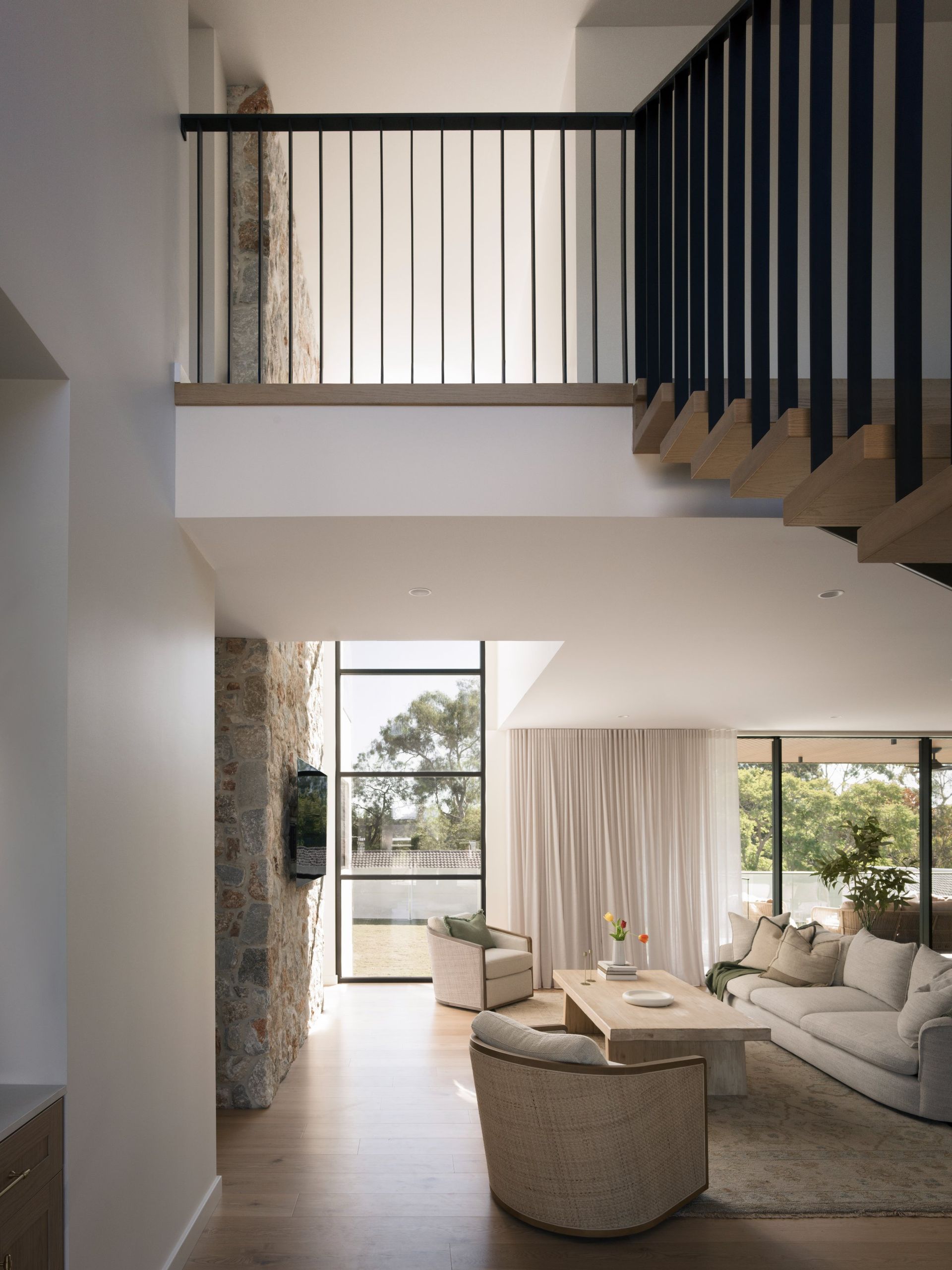 Modern open-plan living room with staircase, floor-to-ceiling window, and neutral furniture — Everyday Interiors in Helensburgh, NSW