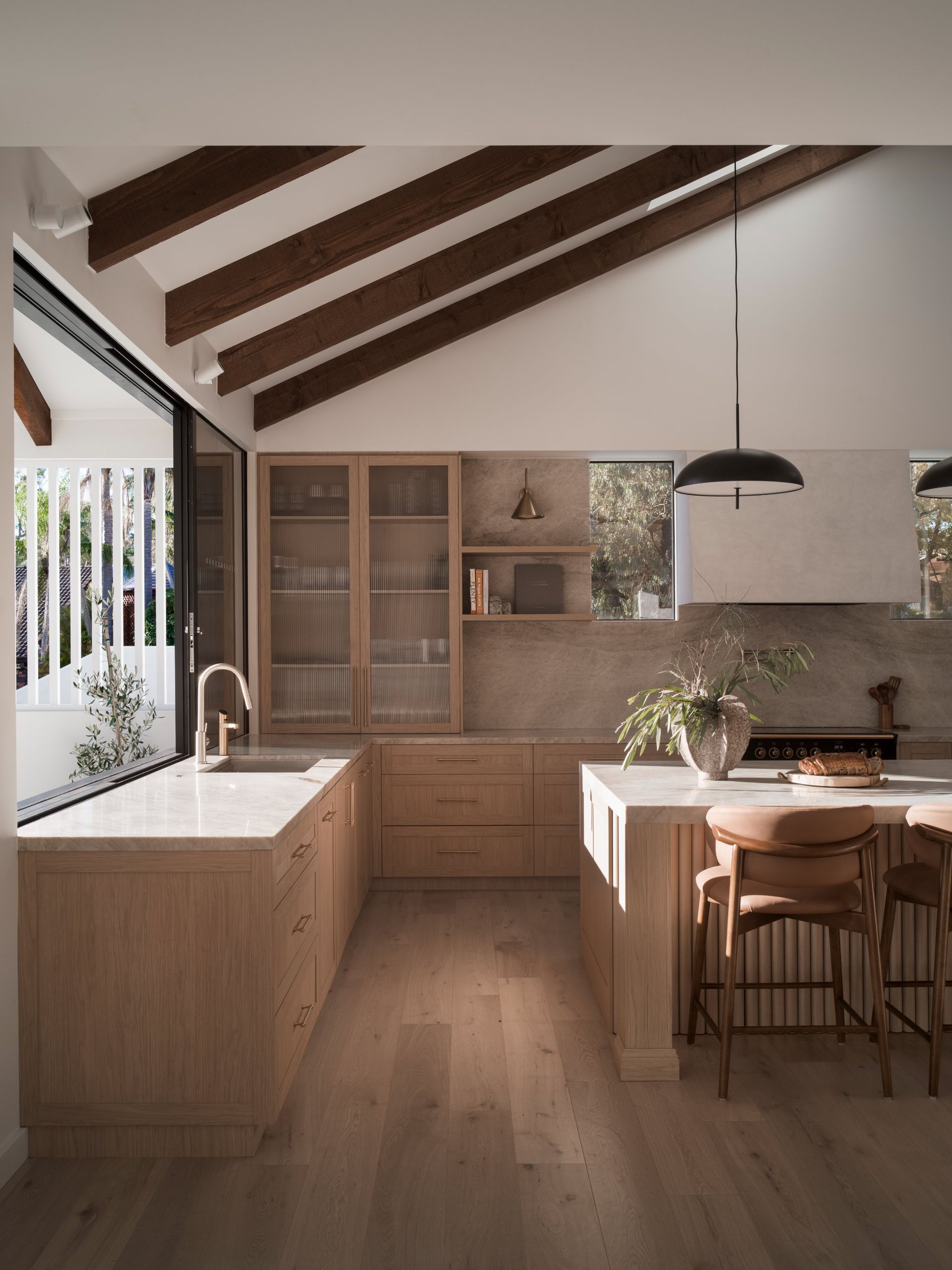 Sunlit modern kitchen with wood beams, island, dining table, and large windows — Everyday Interiors in Helensburgh, NSW