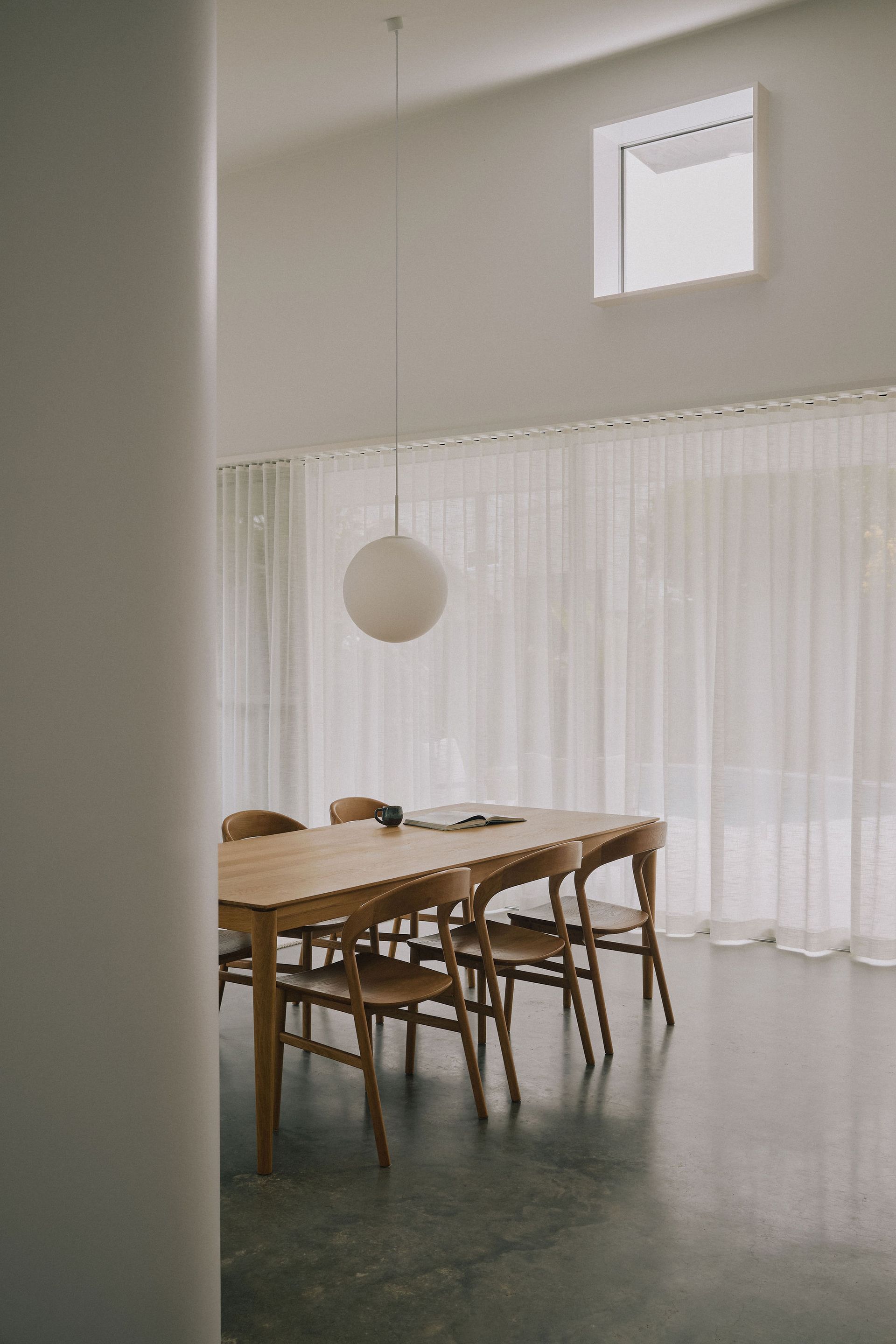Minimal dining room with wooden table, chairs, white curtains, and hanging globe pendant light — Everyday Interiors in Sydney, NSW