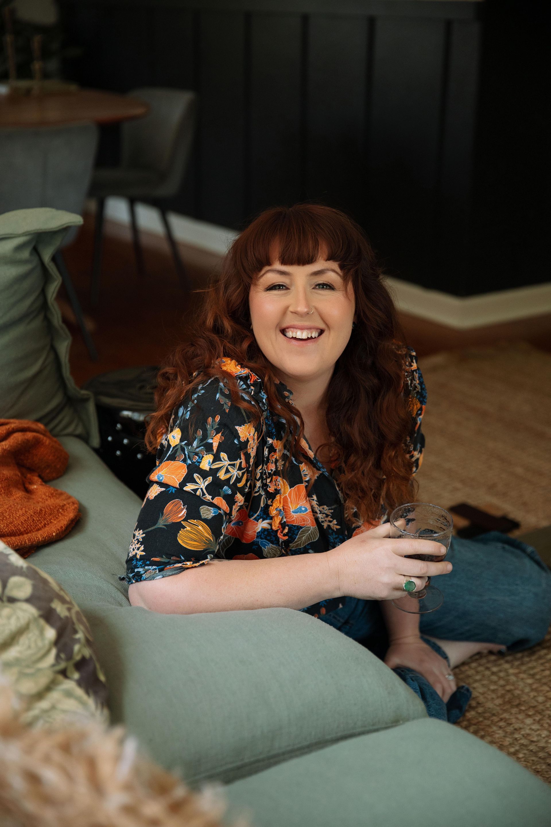 Smiling Person Sitting On A Couch With A Drink In A Cozy Living Room — Everyday Interiors in Wollongong, NSW