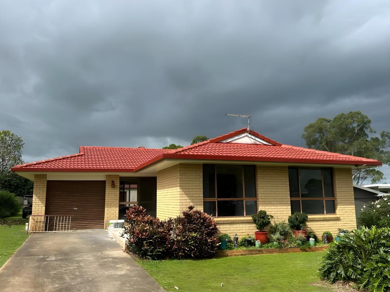 A House With A Red Roof And A Cloudy Sky In The Background — Premier Roofing Solutions In Lennox Head, NSW