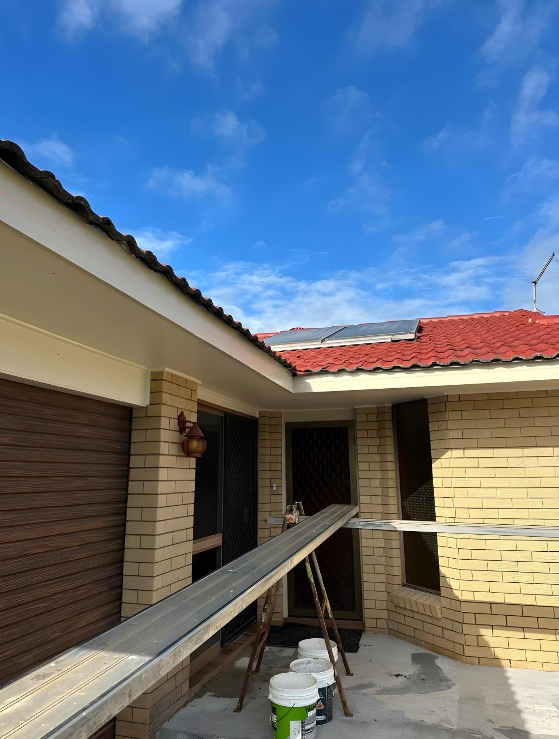 A Brick House With A Red Roof Is Being Painted — Premier Roofing Solutions In Lennox Head, NSW