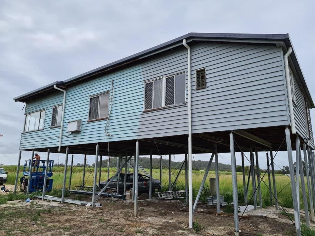 A House Is Sitting On Stilts In The Middle Of A Field — Premier Roofing Solutions In Lennox Head, NSW