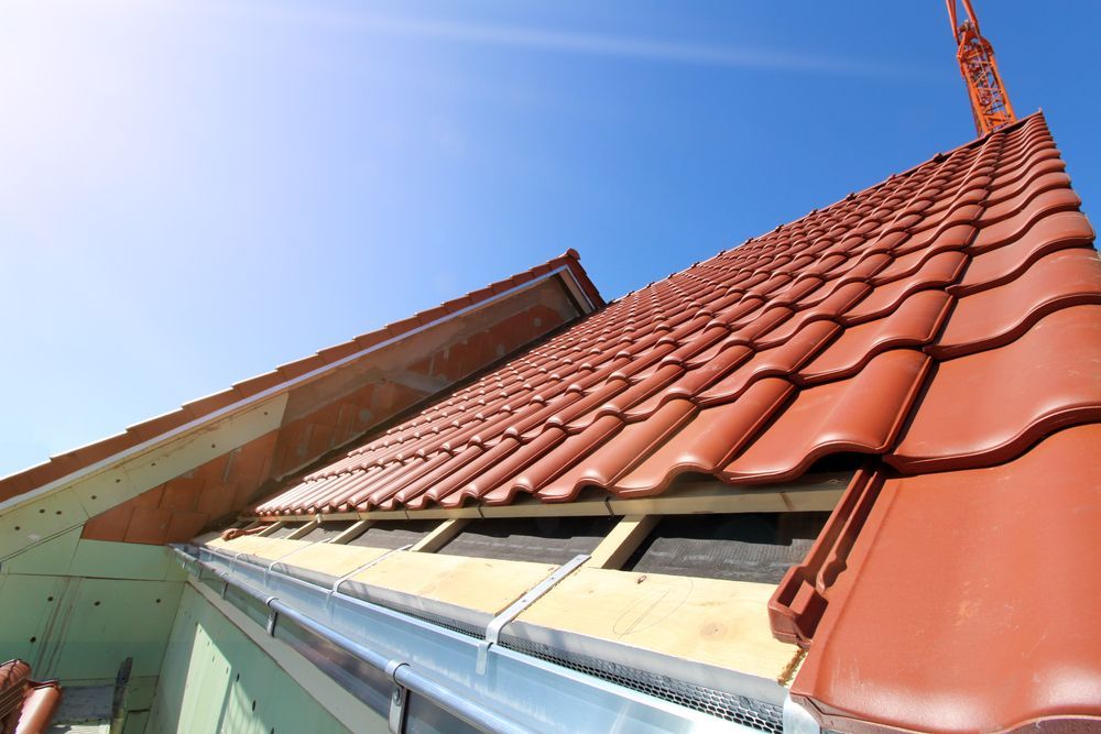 Red tile roof in progress with visible gutter, wooden supports, and bright blue sky