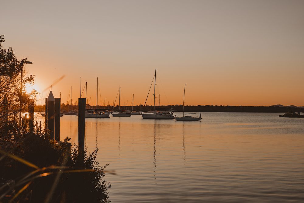 A Sunset Over A Body Of Water With Boats Docked In The Water — Premier Roofing Solutions In Yamba, NSW
