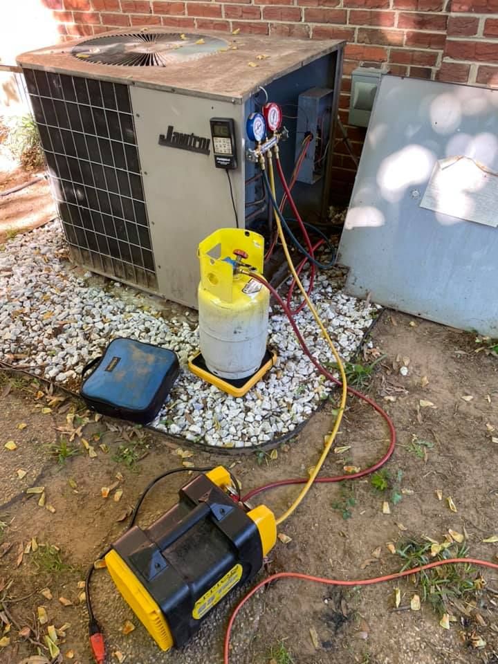 HVAC unit with gauges and hoses connected. Refrigerant tank and vacuum pump visible. Outdoors.