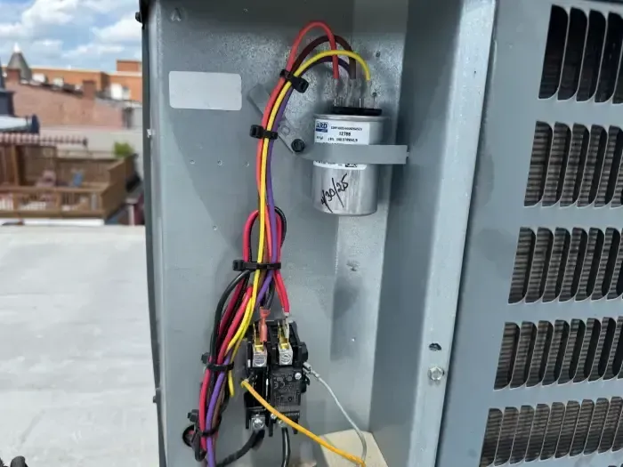 Air conditioning unit control panel with capacitor and wiring on a rooftop.