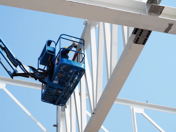 Un uomo in un secchio blu sta lavorando su una struttura metallica.