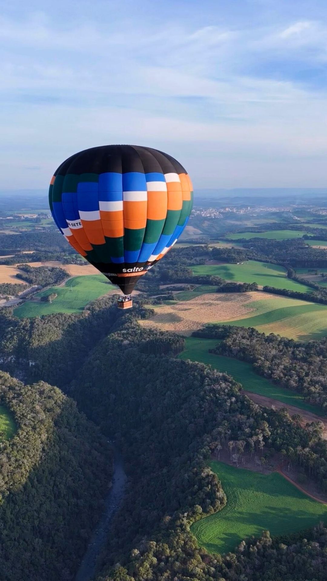 Um balão de ar quente sobrevoa uma paisagem verdejante sob um céu azul.