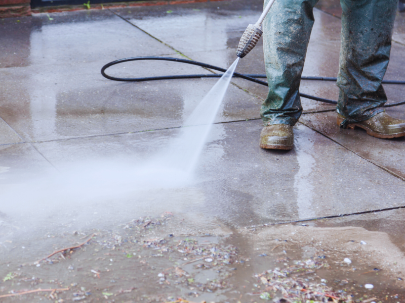 A man is using a high pressure washer to clean a sidewalk.