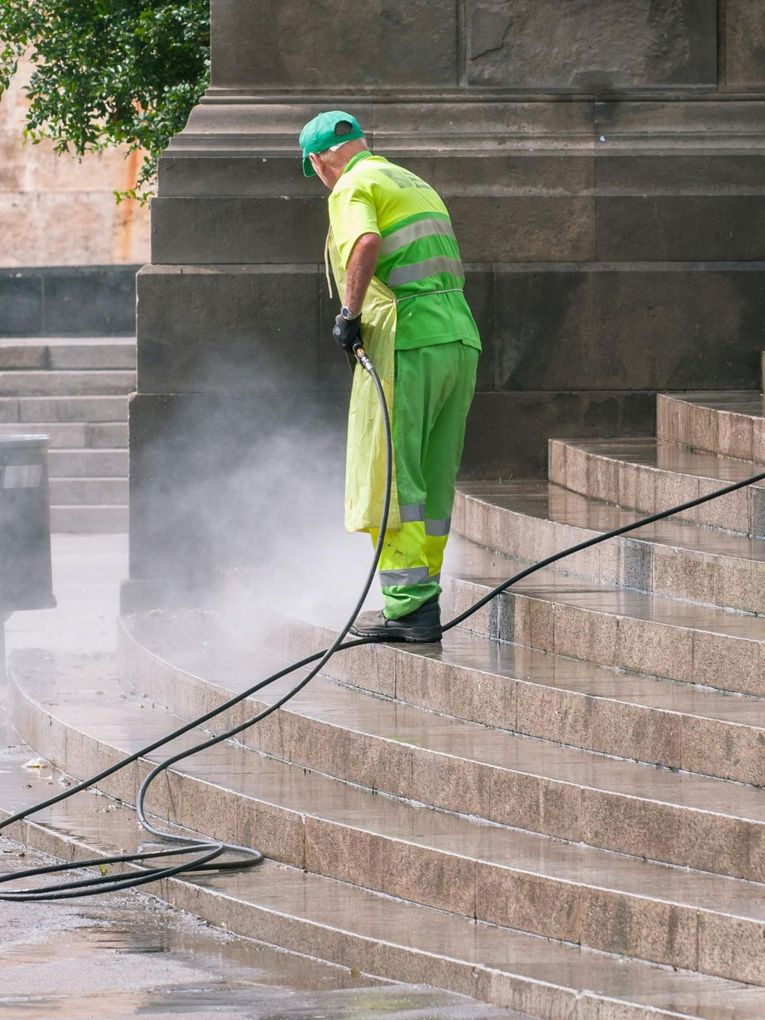 A man is cleaning the steps of a building with a high pressure washer.