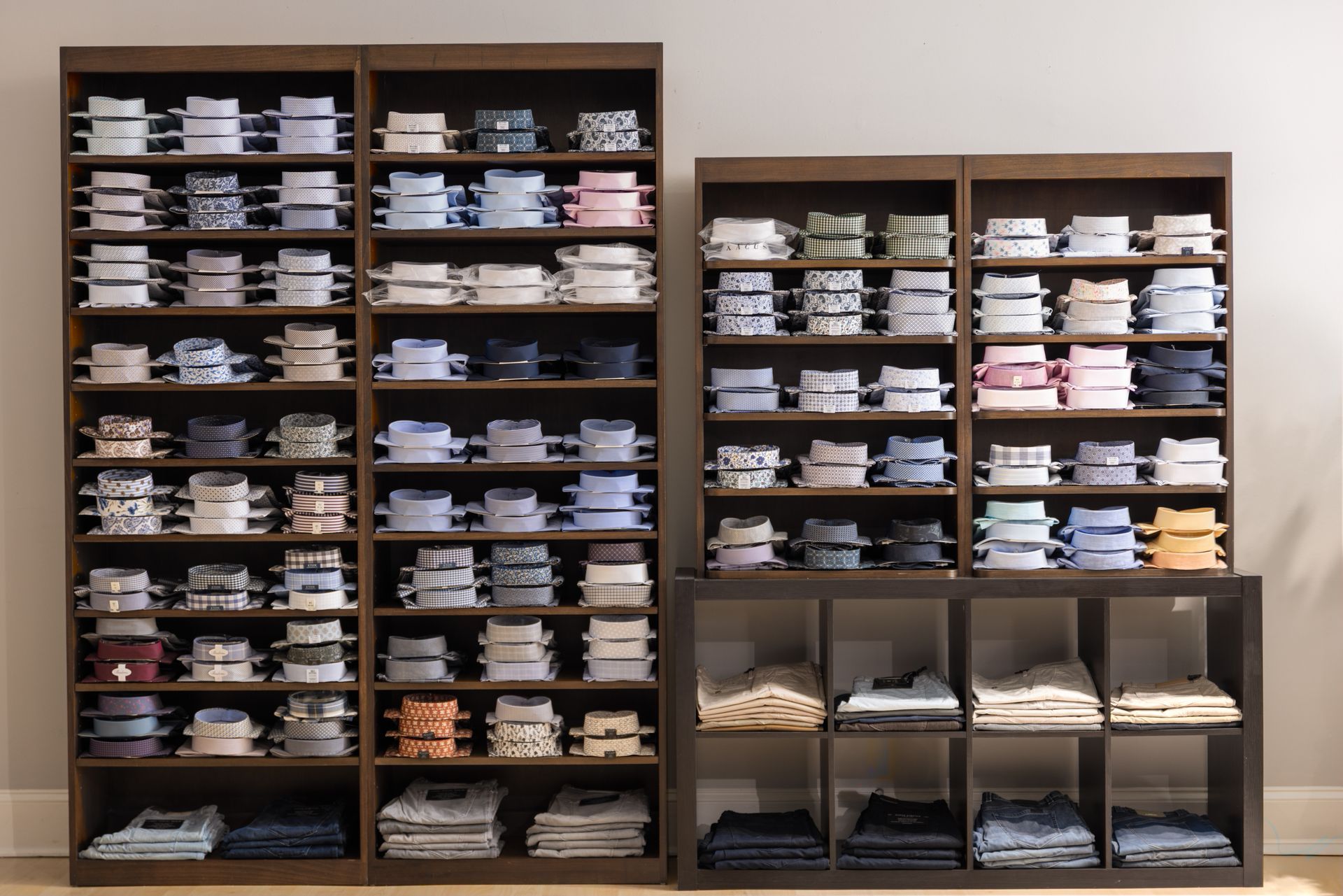 Dark wooden shelves filled with neatly folded and stacked shirts, jeans, and cubby-style storage.