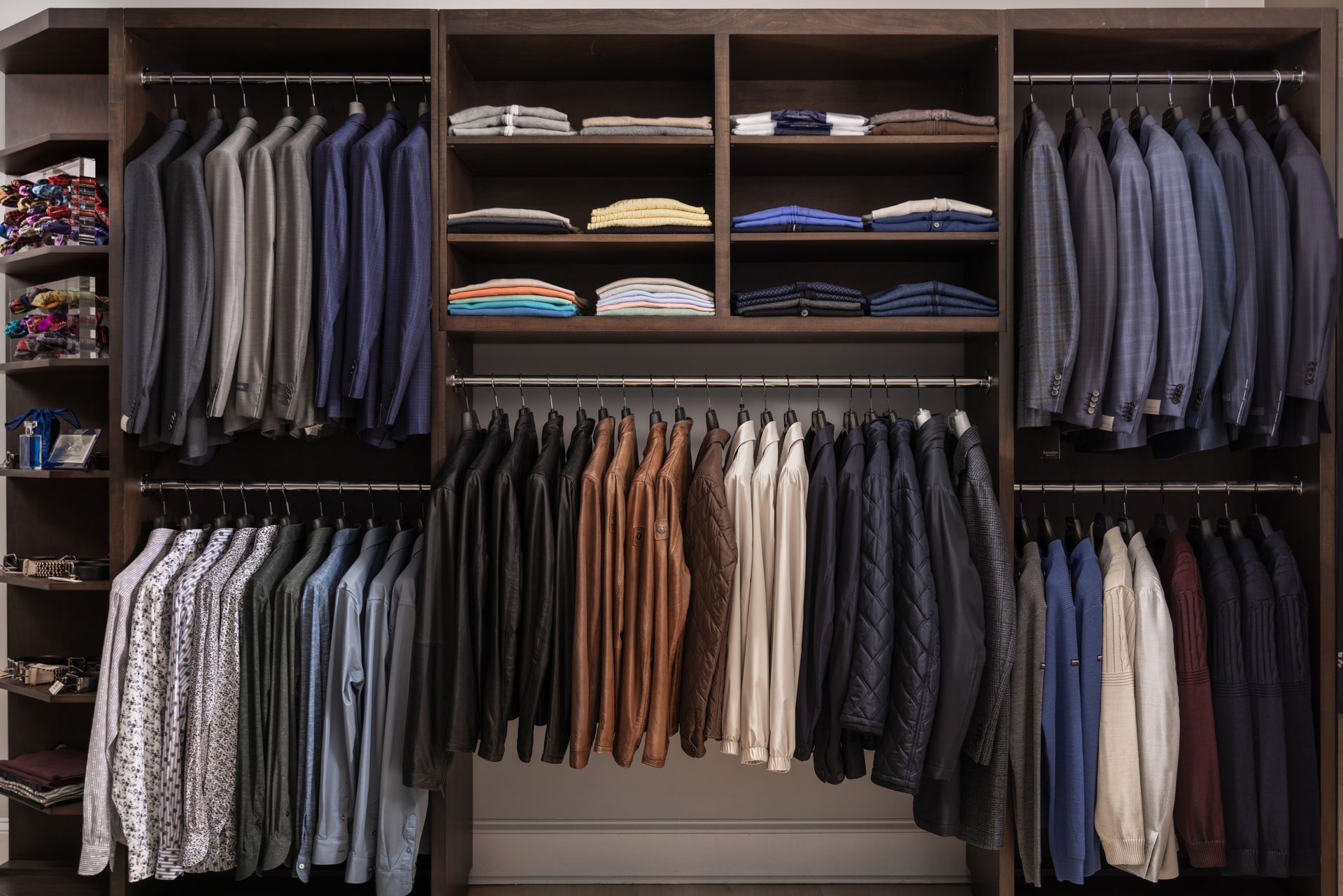 A well-organized closet with suits, shirts, and folded items in various colors on shelves and hanging rods.
