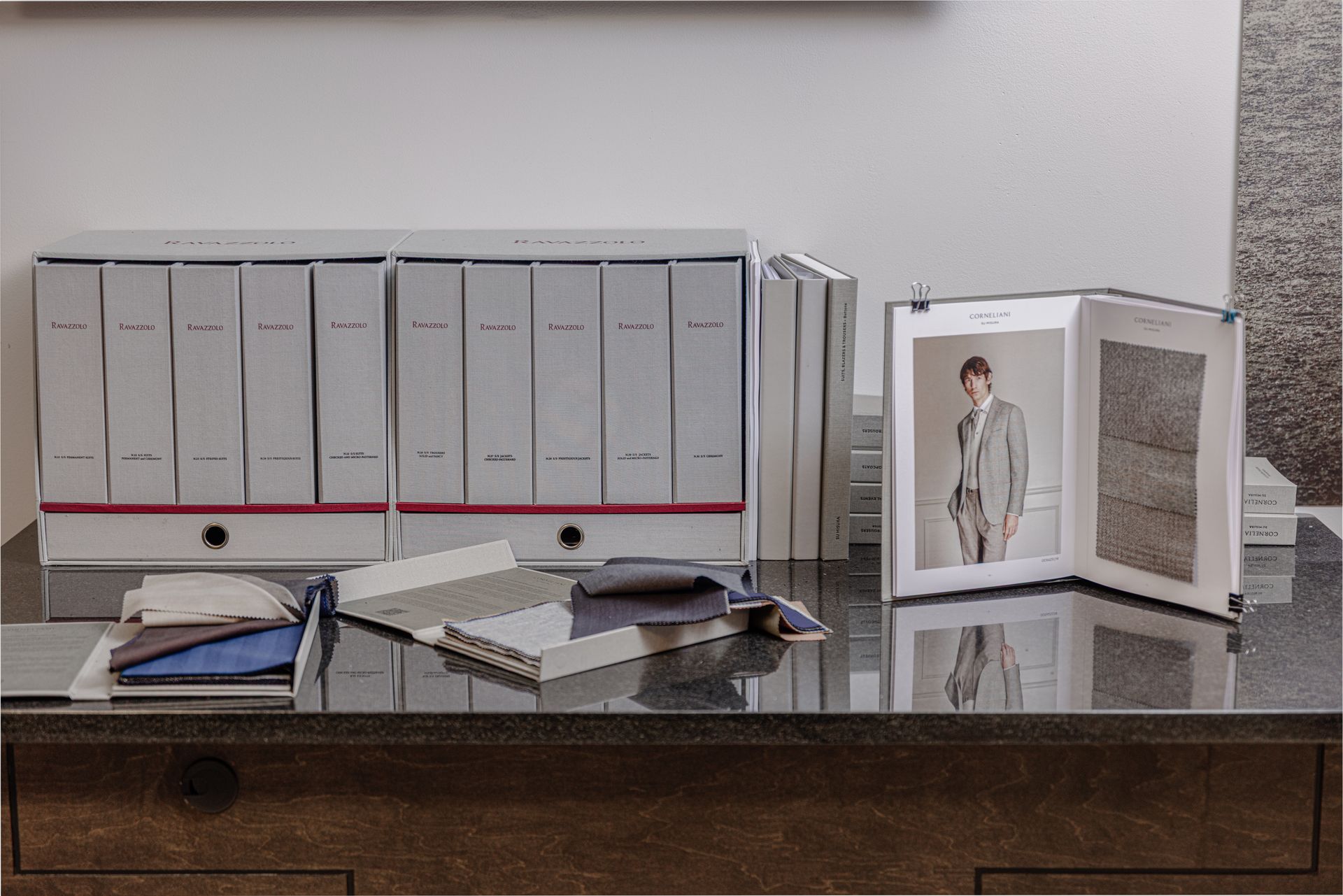 Desk with binders, fabric samples, and a catalog open to a photo of a person in a suit.