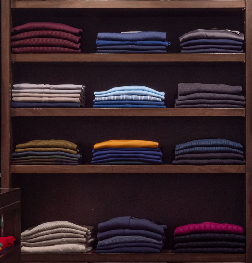 Shelves stocked with neatly folded clothing in various colors, displayed in a store setting.