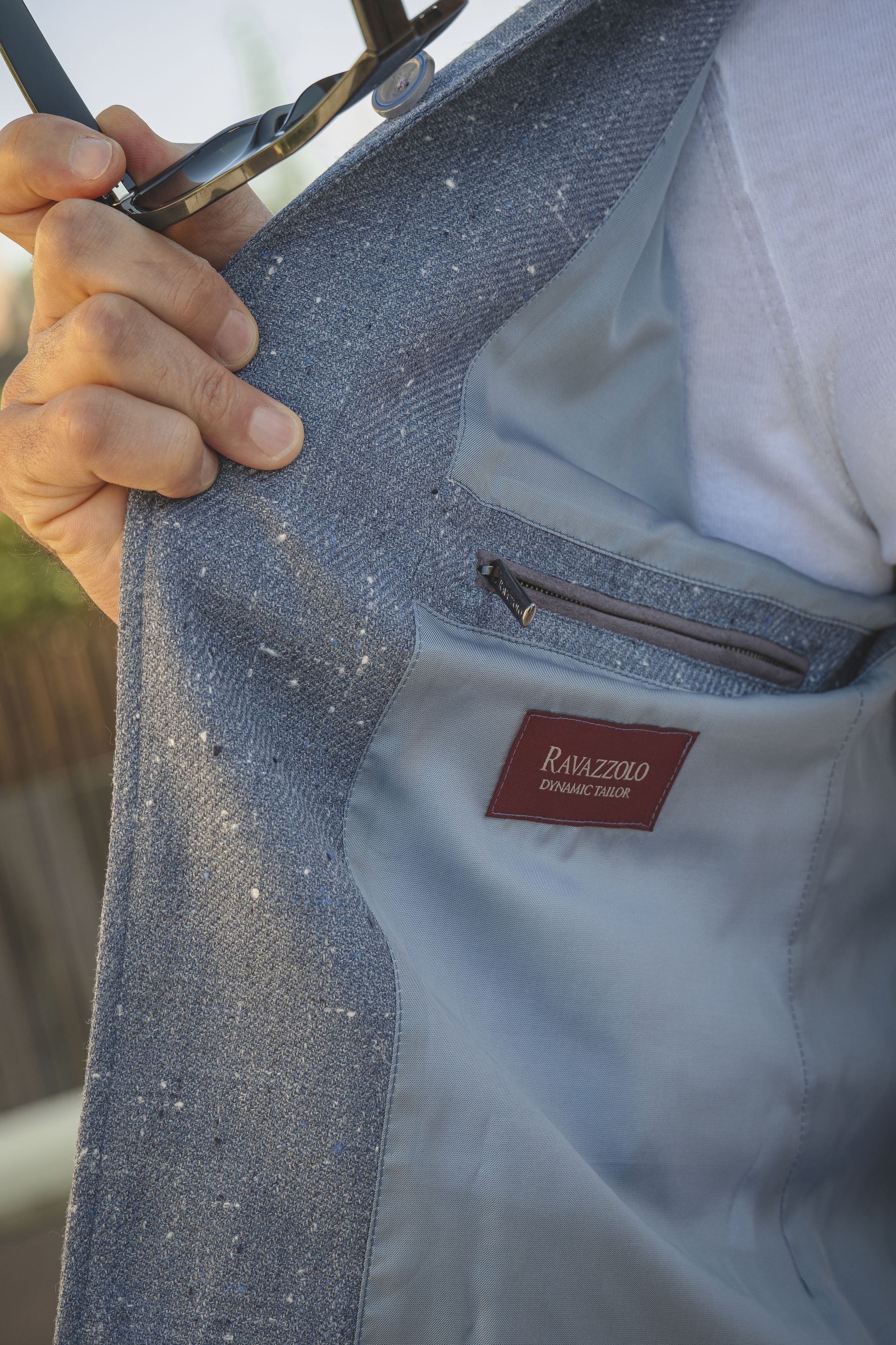 Person holding open a gray tweed jacket, revealing a light blue lining and interior pocket.