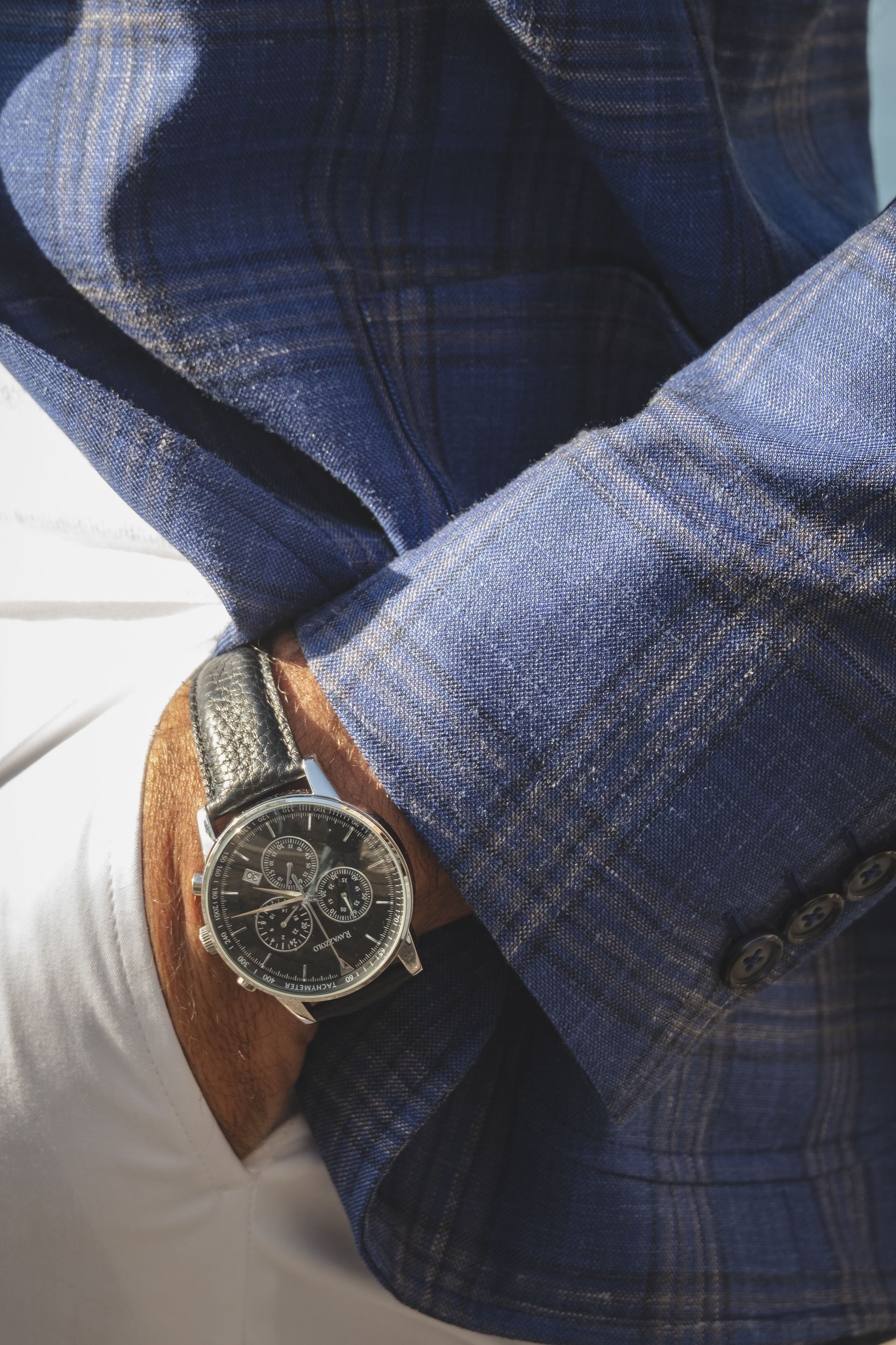 Man's wrist with watch, blue plaid jacket, white pants.