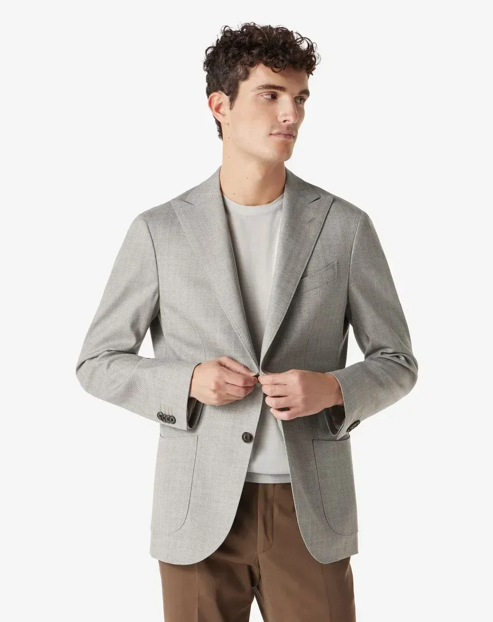 Man in a gray blazer and brown pants, buttoning the jacket. Light background.