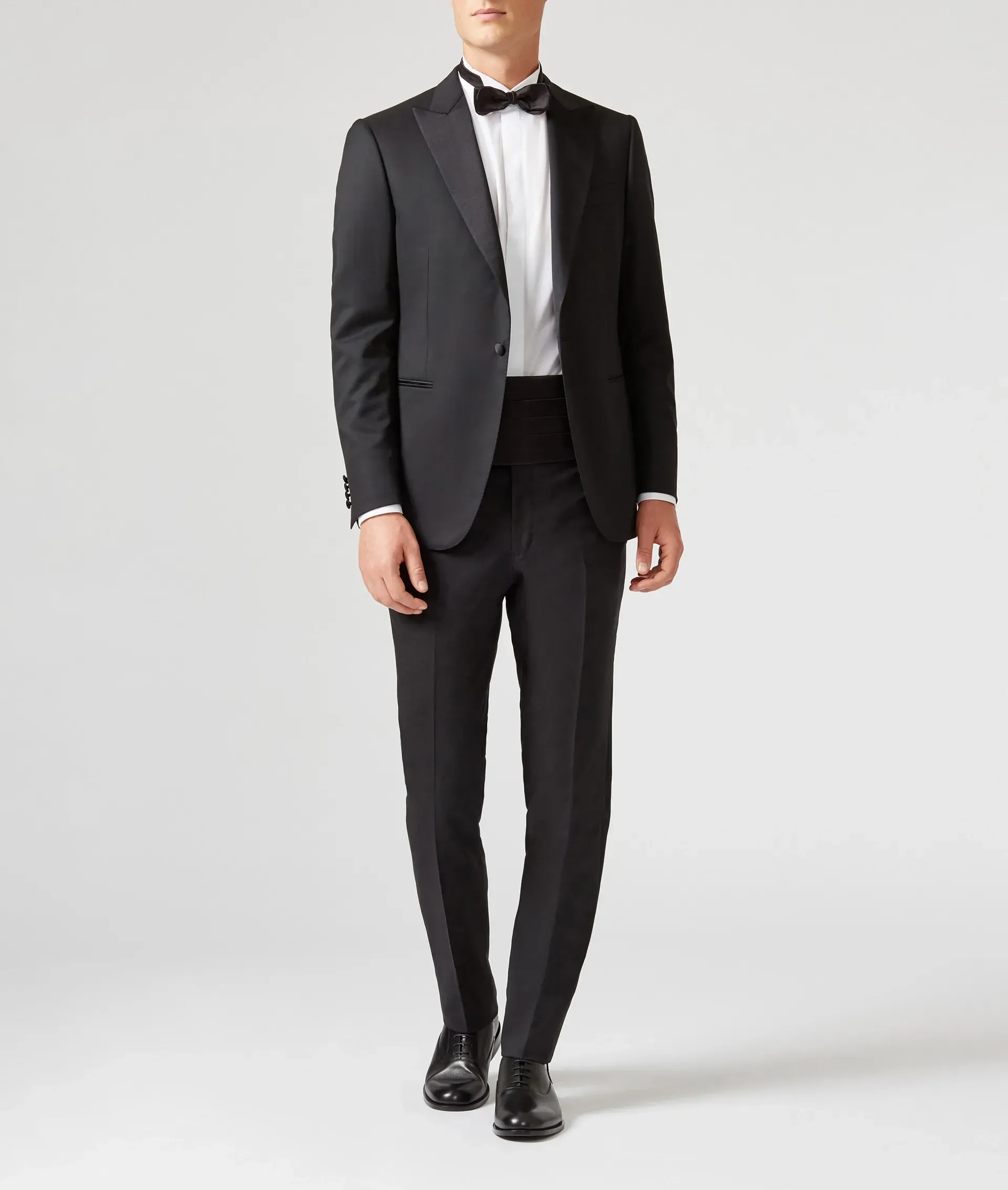 Man in black tuxedo, bow tie, white shirt, and black dress shoes, standing.