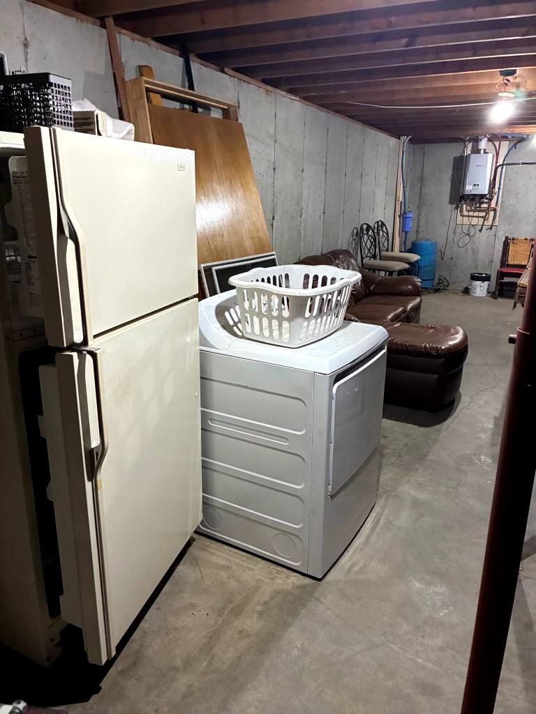 Basement storage area with a white refrigerator, laundry washer, and brown couch under exposed ceiling beams