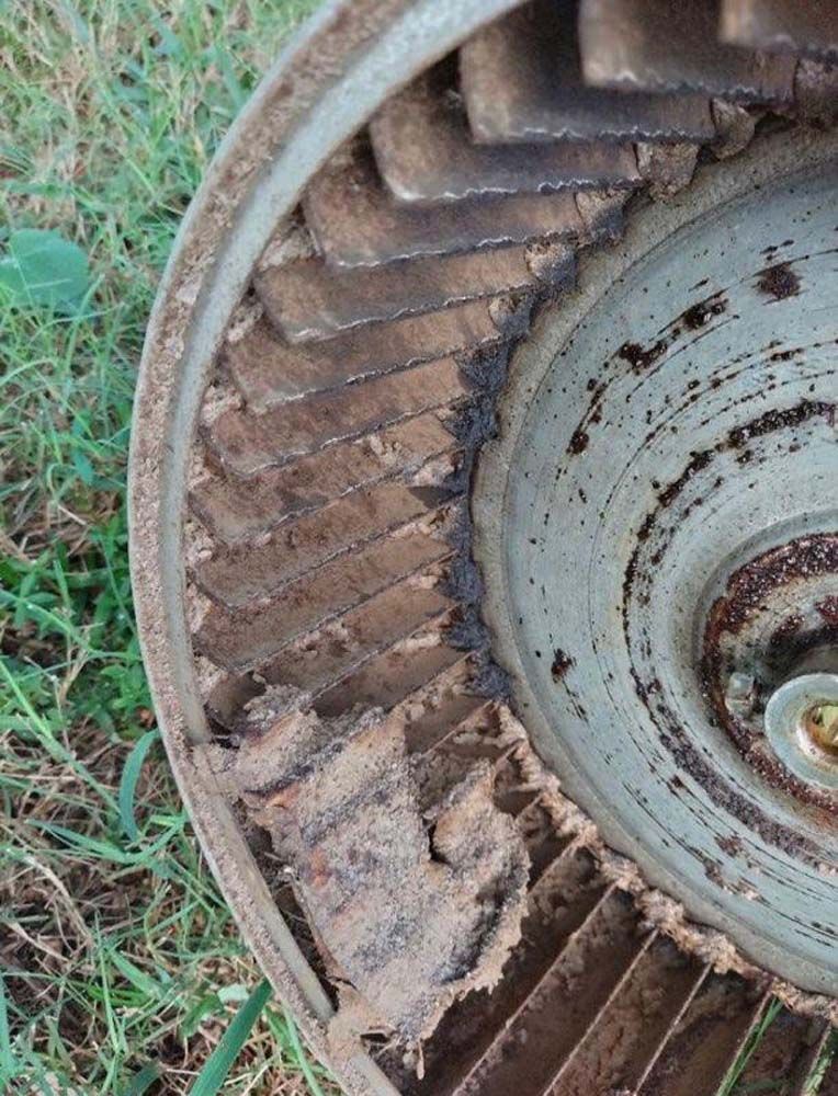 A close up of a rusty fan sitting in the grass.