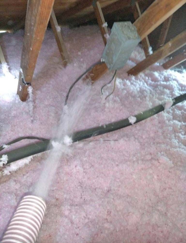 A hose is being used to blow insulation into an attic.