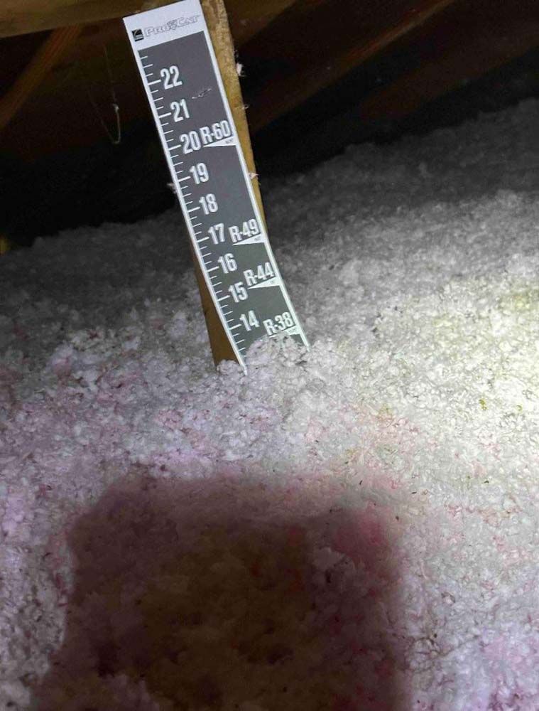 A ruler is sitting on top of a pile of insulation in an attic.