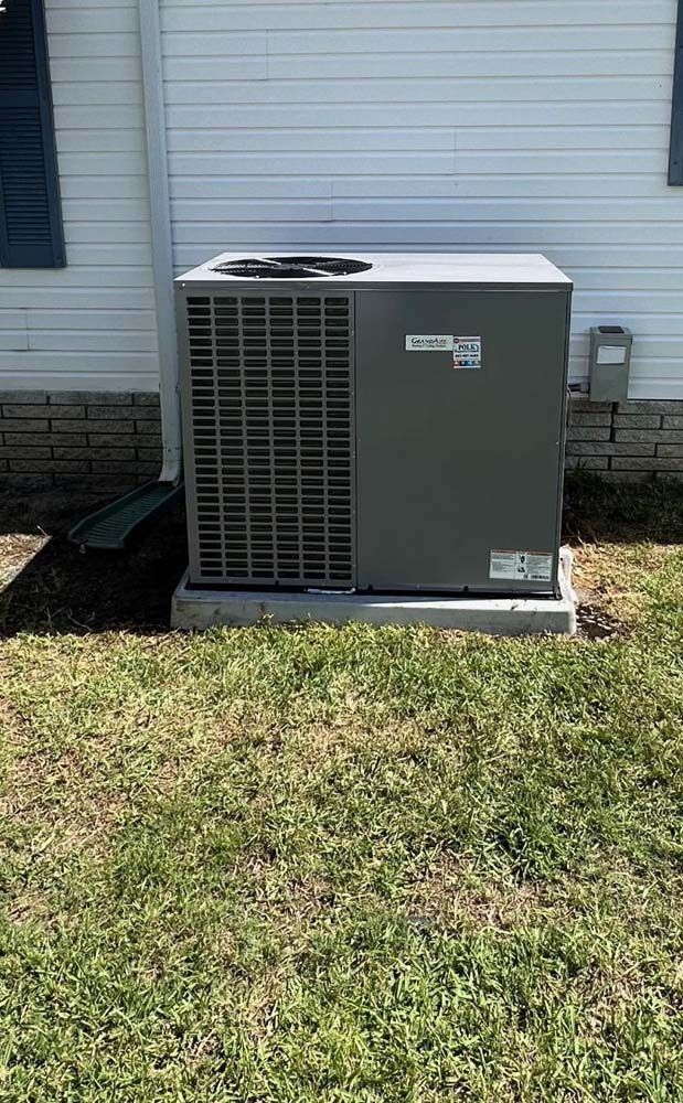 A large air conditioner is sitting in the grass in front of a house.