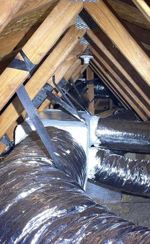 A bunch of ducts are hanging from the ceiling of an attic.