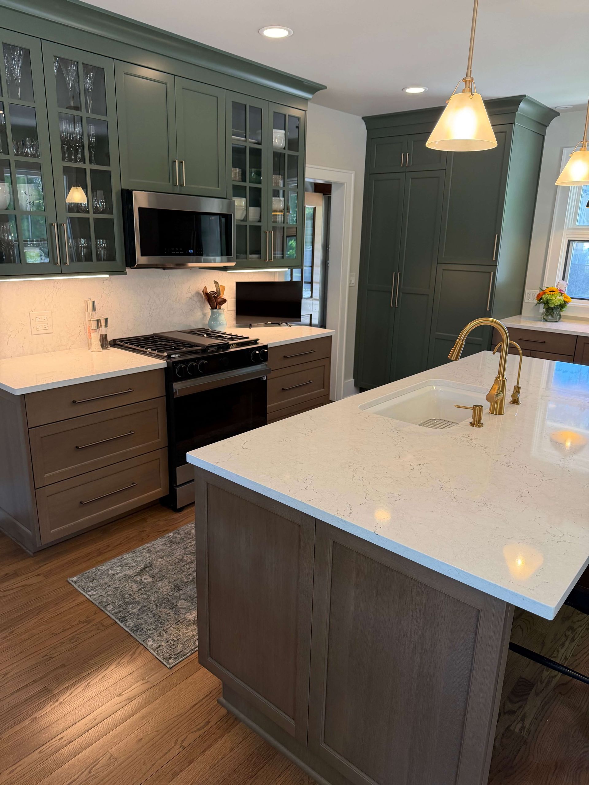 Bright modern kitchen remodeling with island, pendant lights, wood floors, and adjoining living area with fireplace in Glenview, IL.