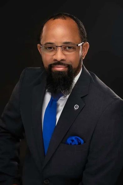 A man with a beard and glasses is wearing a suit and tie.