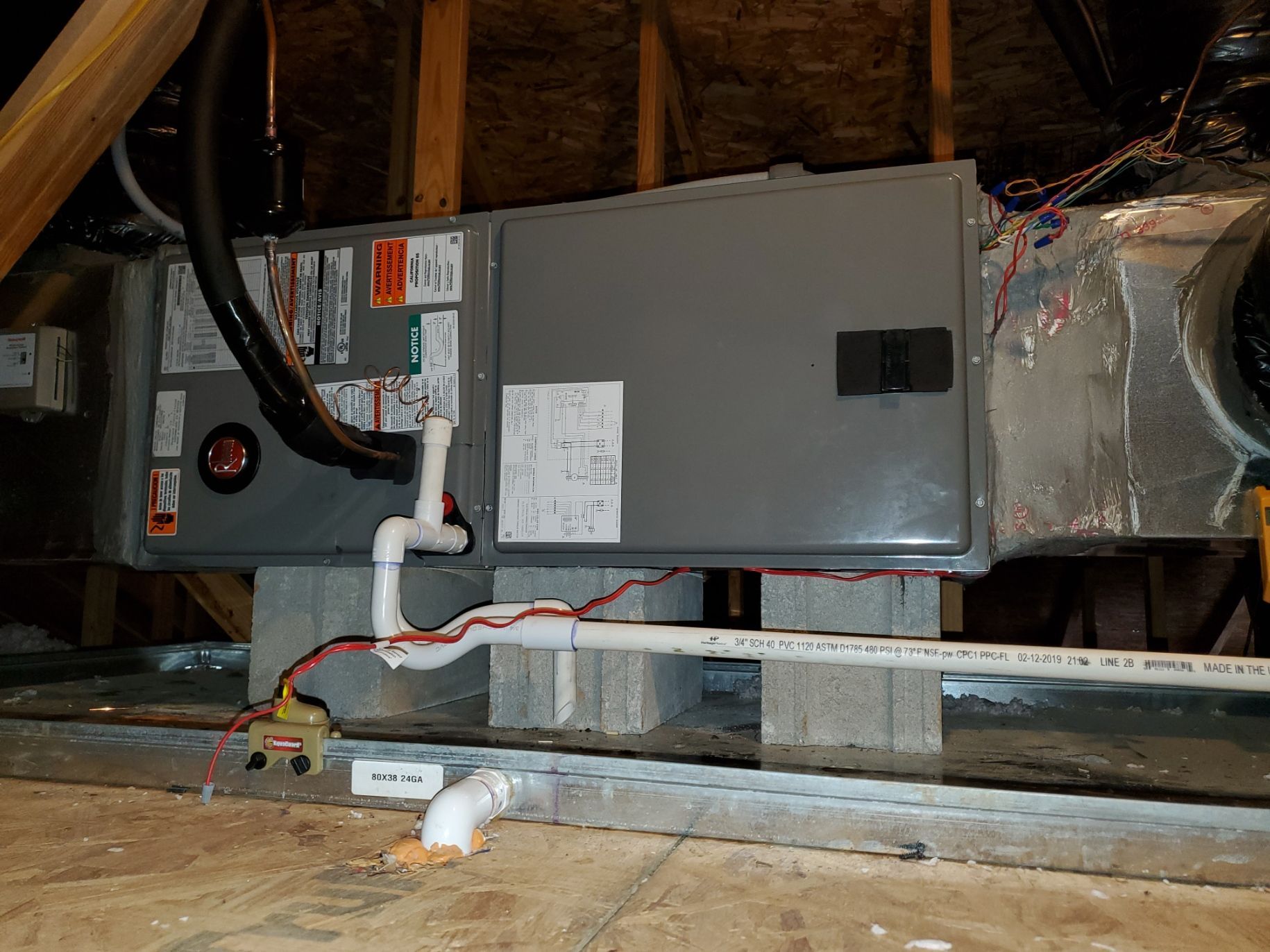 Furnace unit on cinder blocks in an attic. Piping and wiring visible.