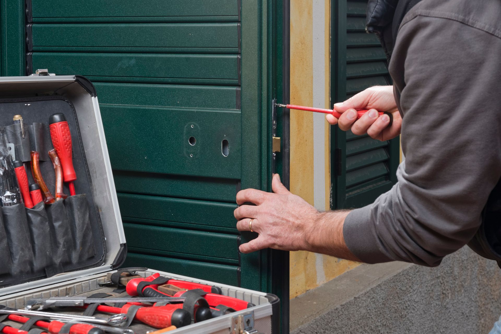 Locksmith repairing metal door lock with screwdriver and tool kit for home security.