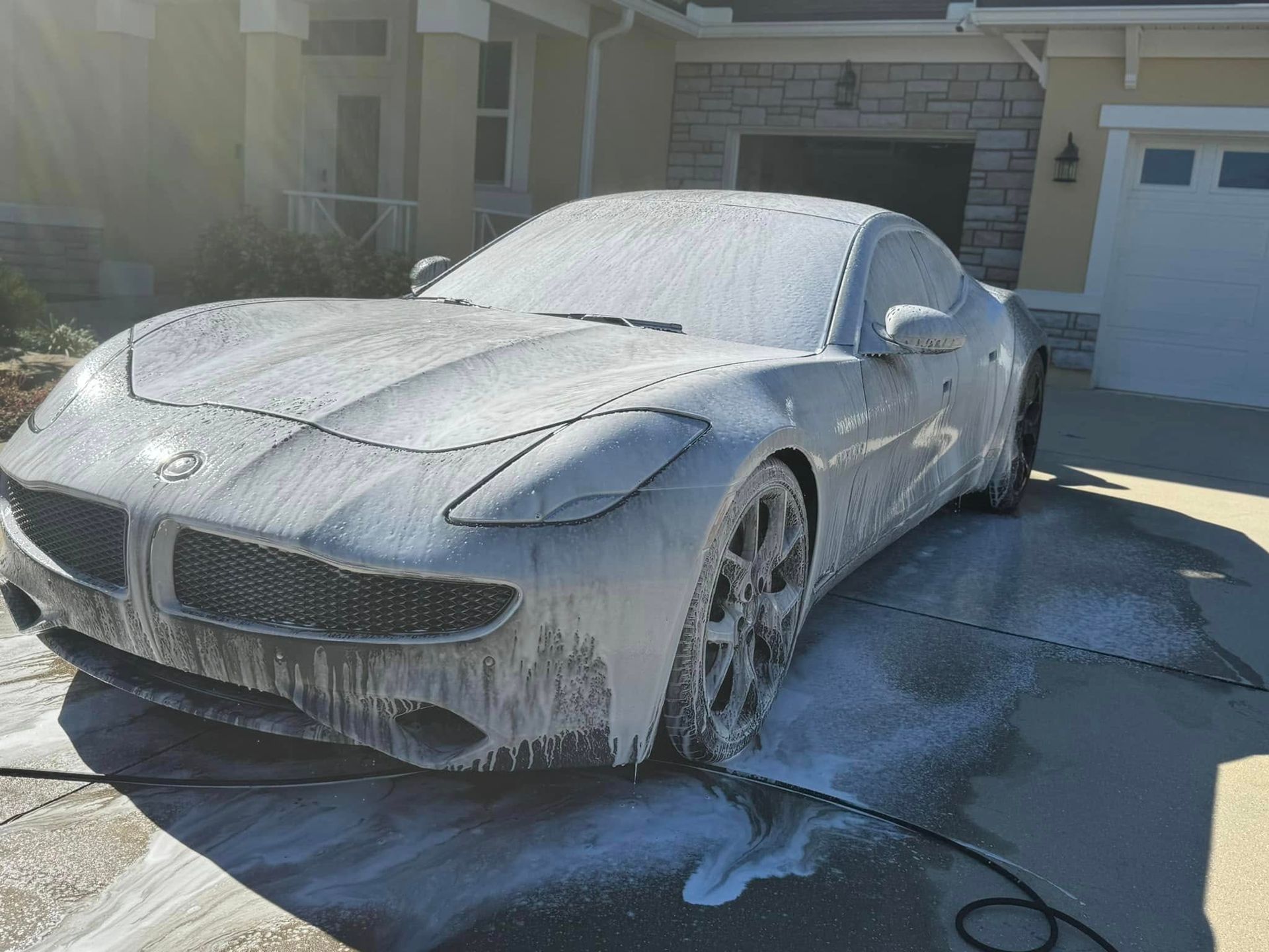 A blue tesla model x with its trunk open is parked in a driveway.