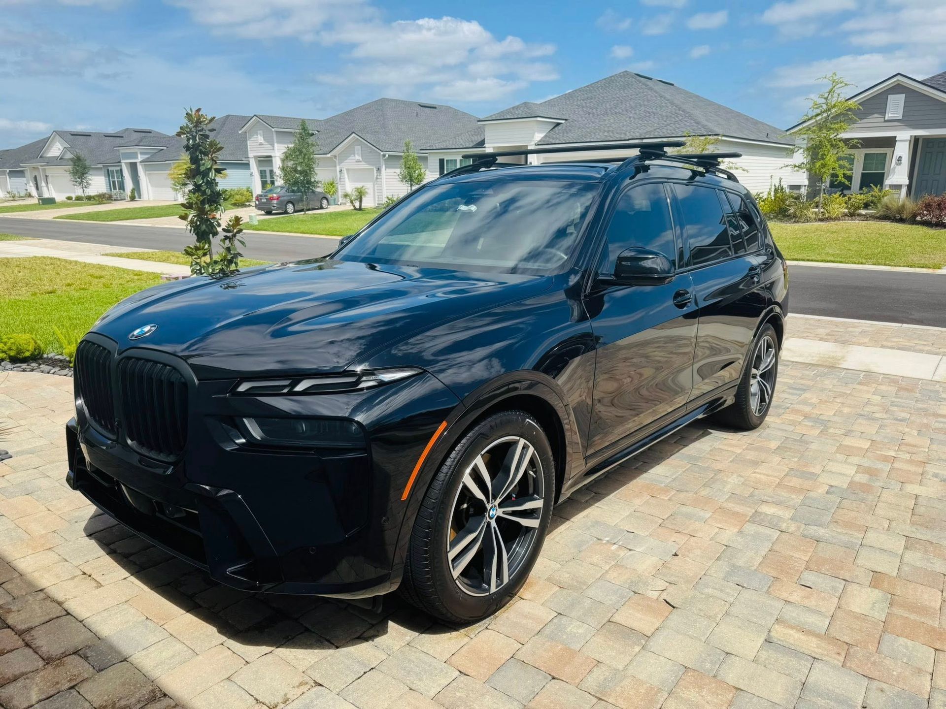 A black bmw x7 is parked on a brick driveway in front of a house.
