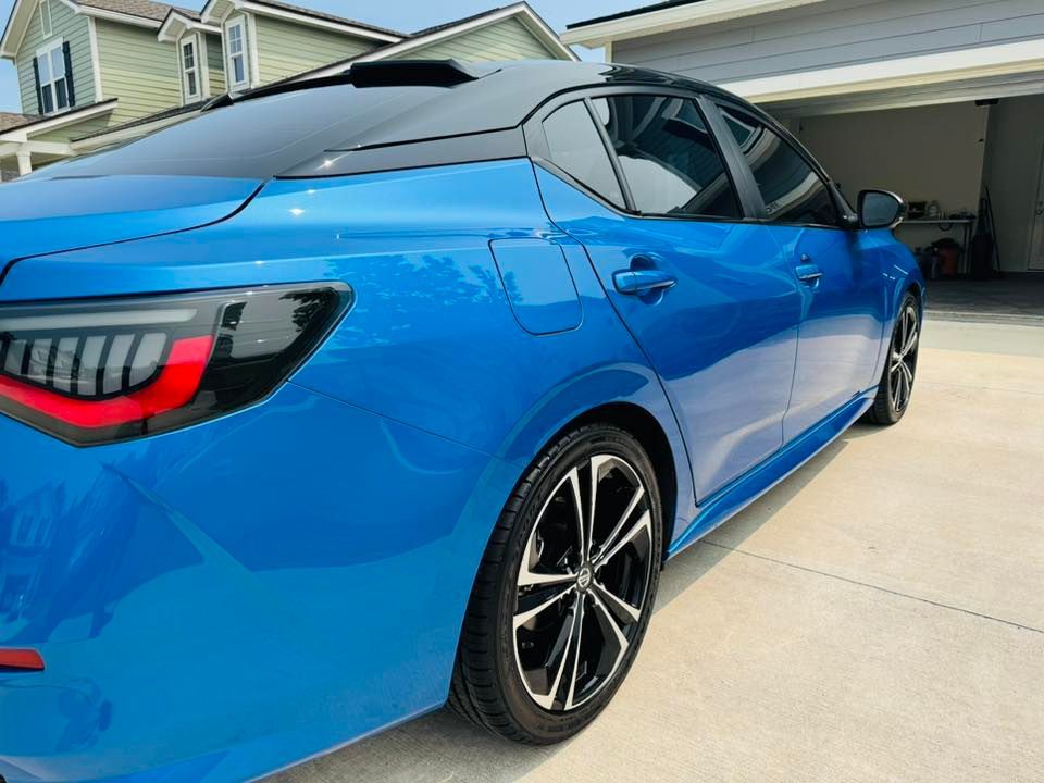 A blue car is parked in a driveway in front of a house.