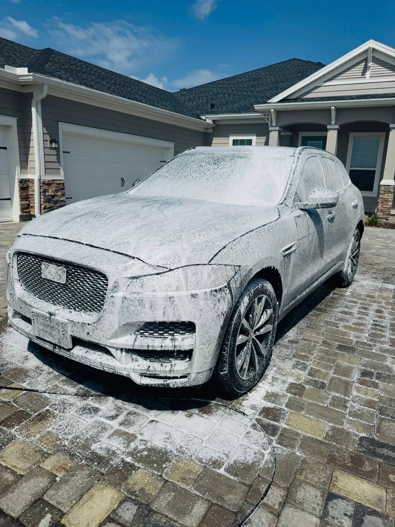 A white car is covered in foam in front of a house.