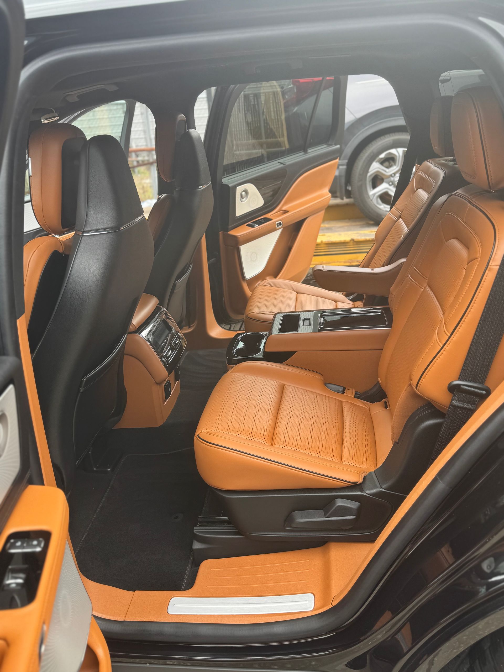 A black car with brown leather seats is parked in front of a house.