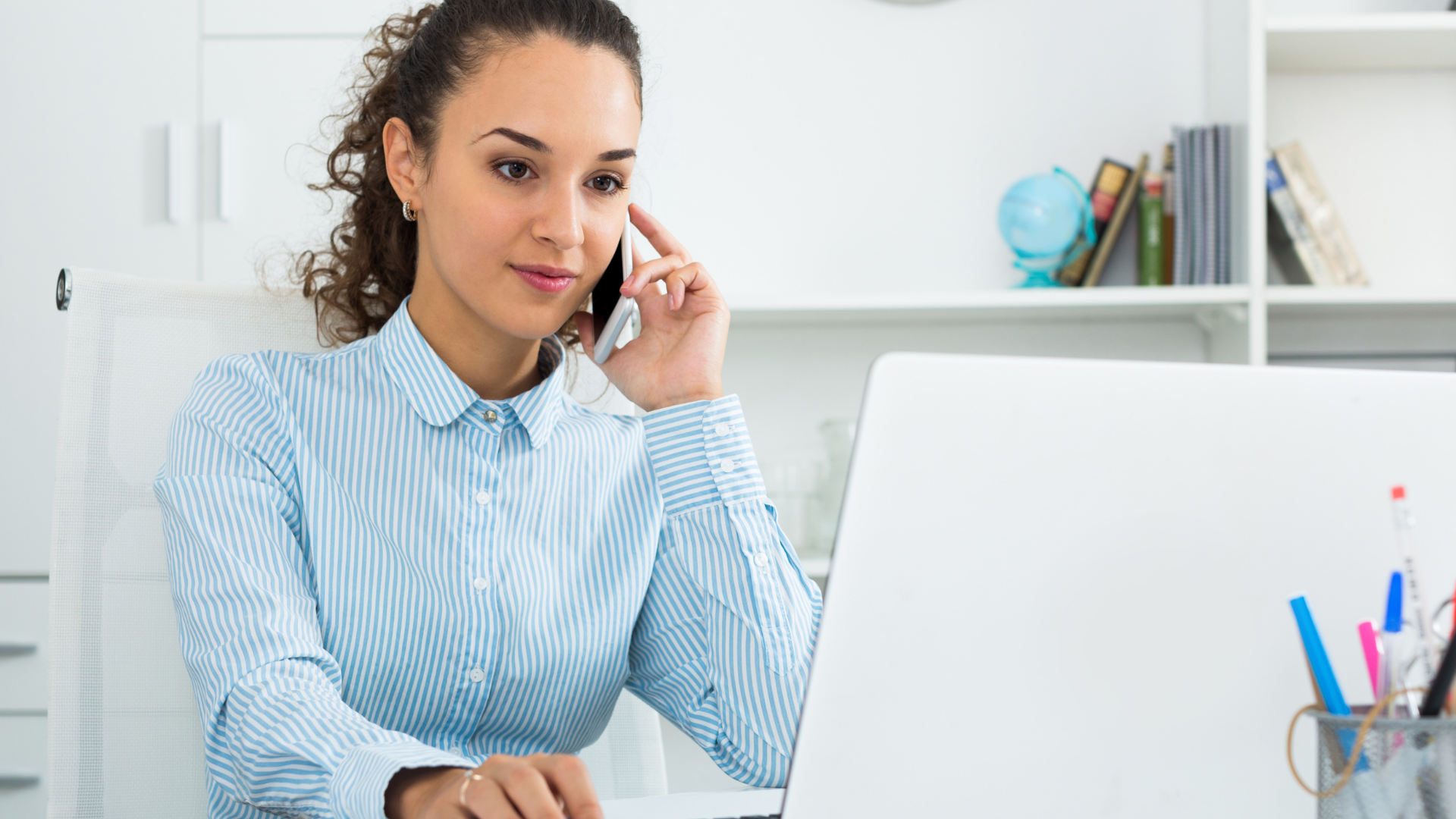 Woman on a phone call working at a laptop in a bright office