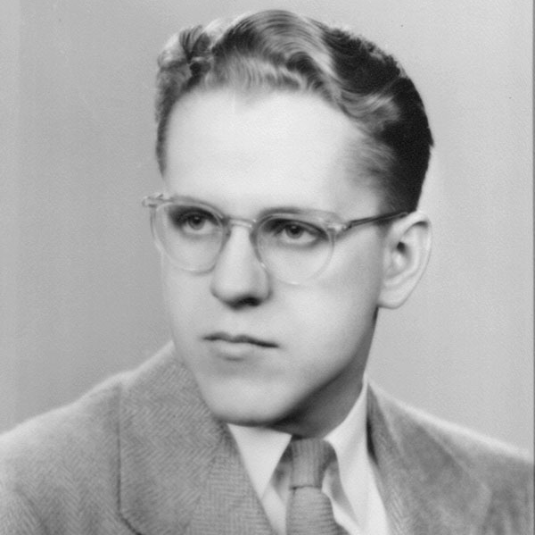 A young man with glasses in a suit poses for a black and white portrait.