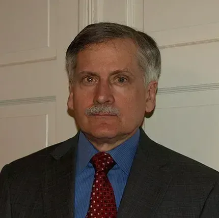 A man with graying hair and a mustache in a suit and tie, looking directly at the viewer.