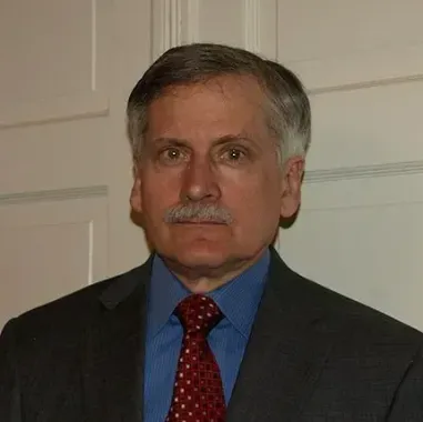 A man with graying hair and a mustache in a suit and tie, looking directly at the viewer.