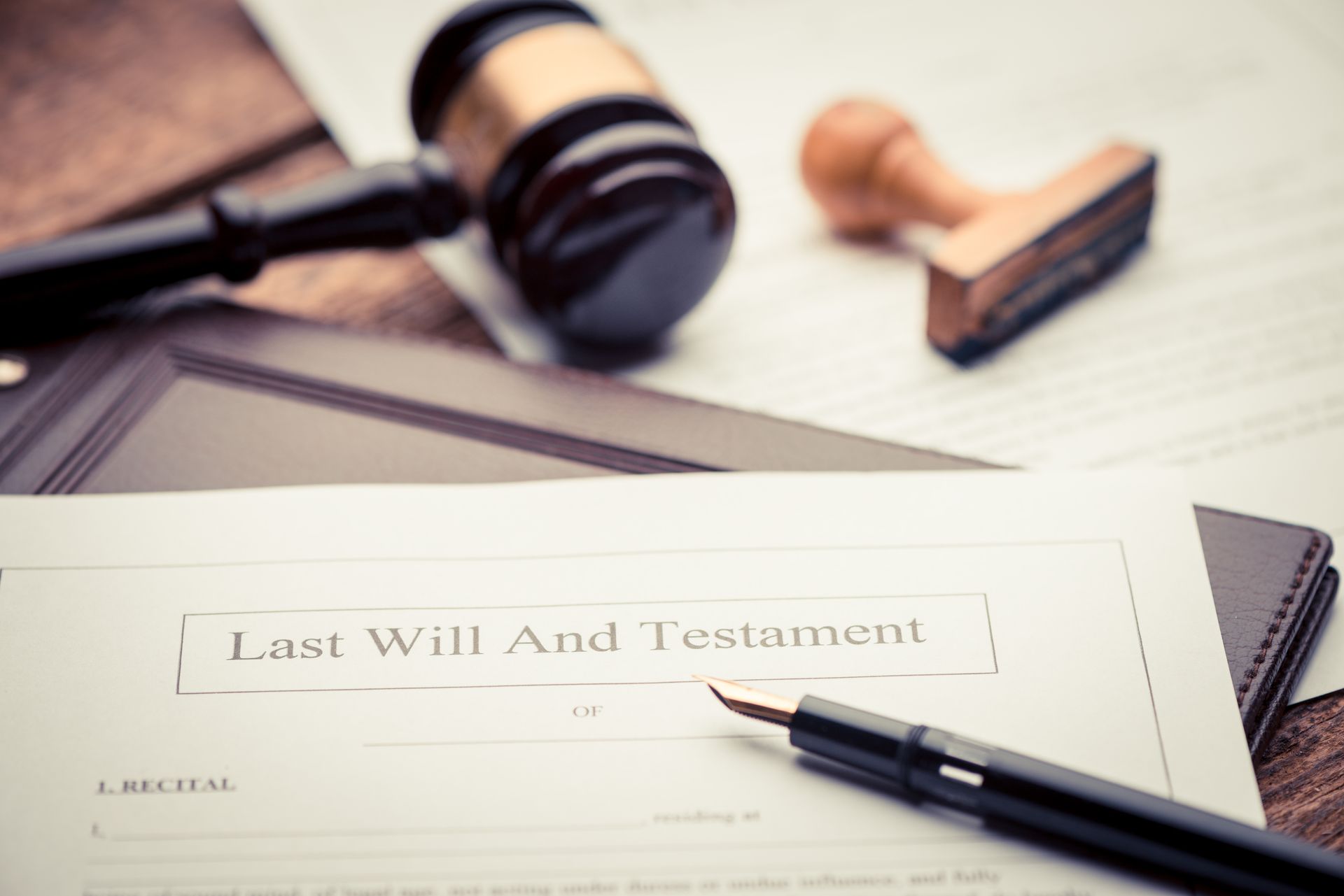 A Last Will and Testament document with a pen, gavel, and stamp on a wooden surface.