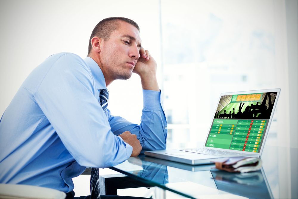 A man in a blue shirt and tie is sitting in front of a laptop computer