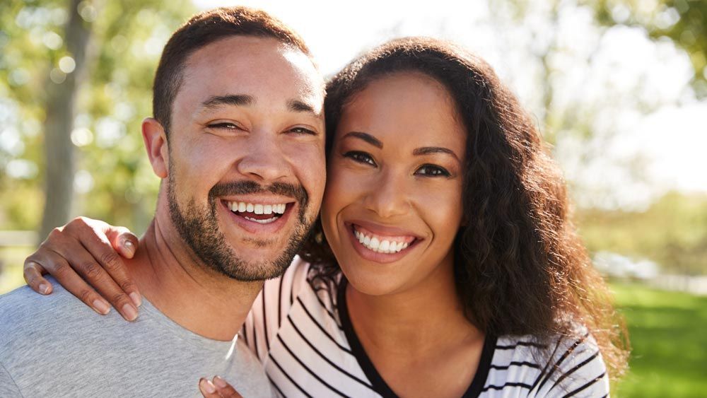 A man and a woman are posing for a picture in a park.