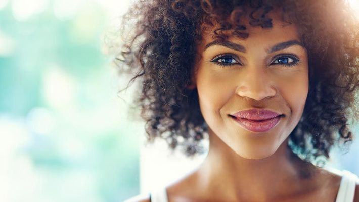 A woman with curly hair is smiling and looking at the camera.