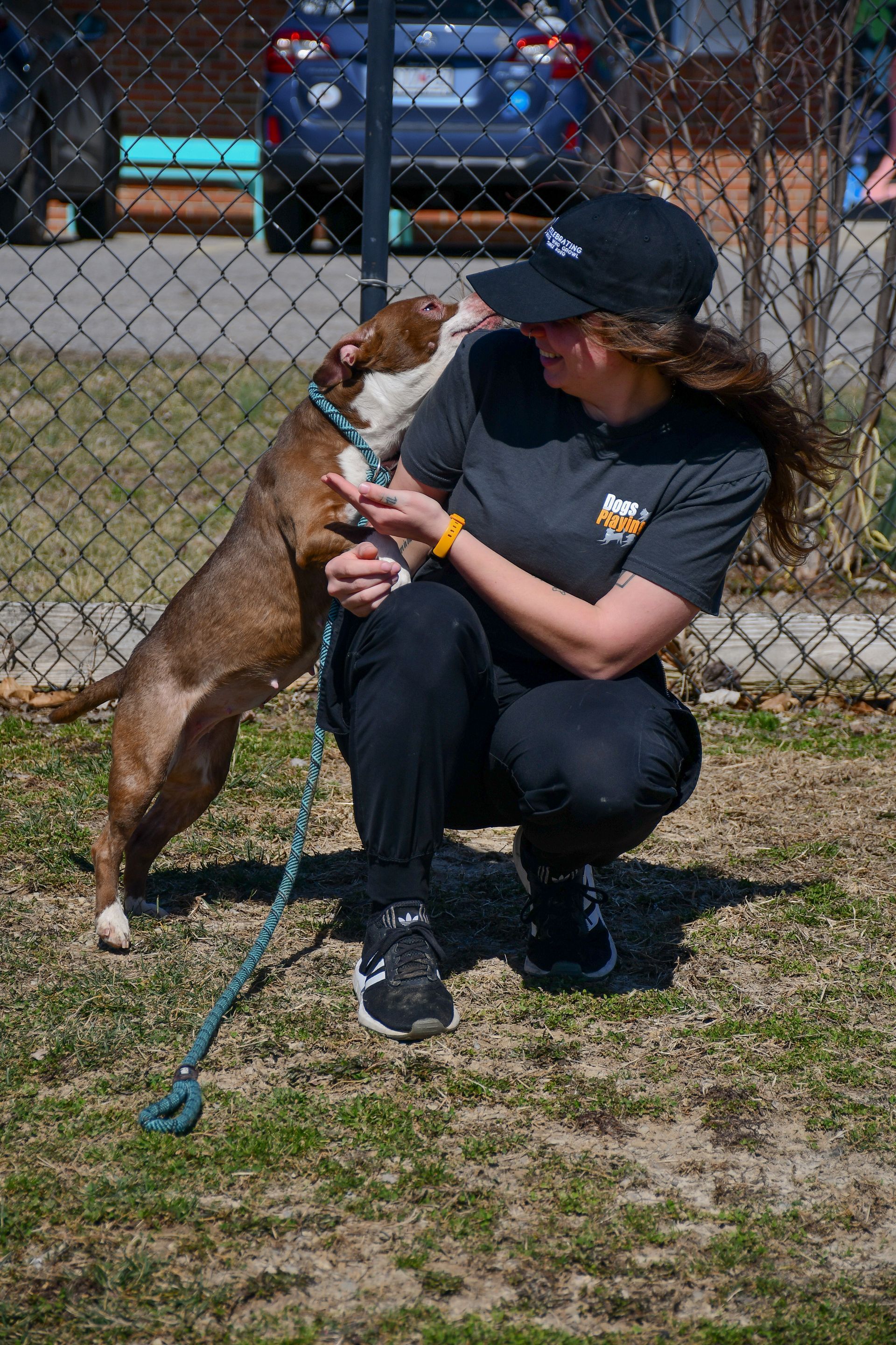 A woman is kneeling down next to a dog on a leash.