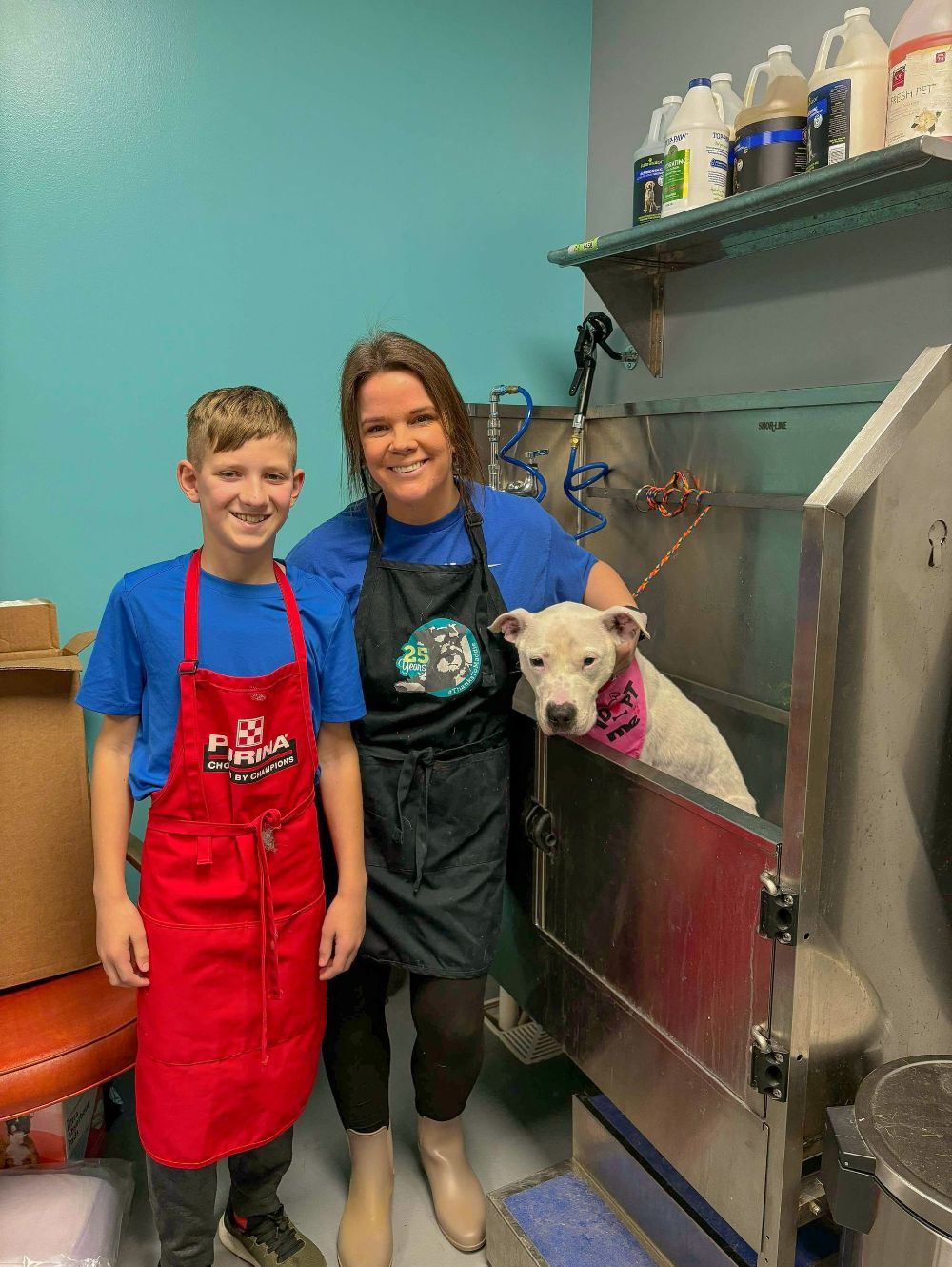 A boy and a woman are standing next to a dog in a bathtub.