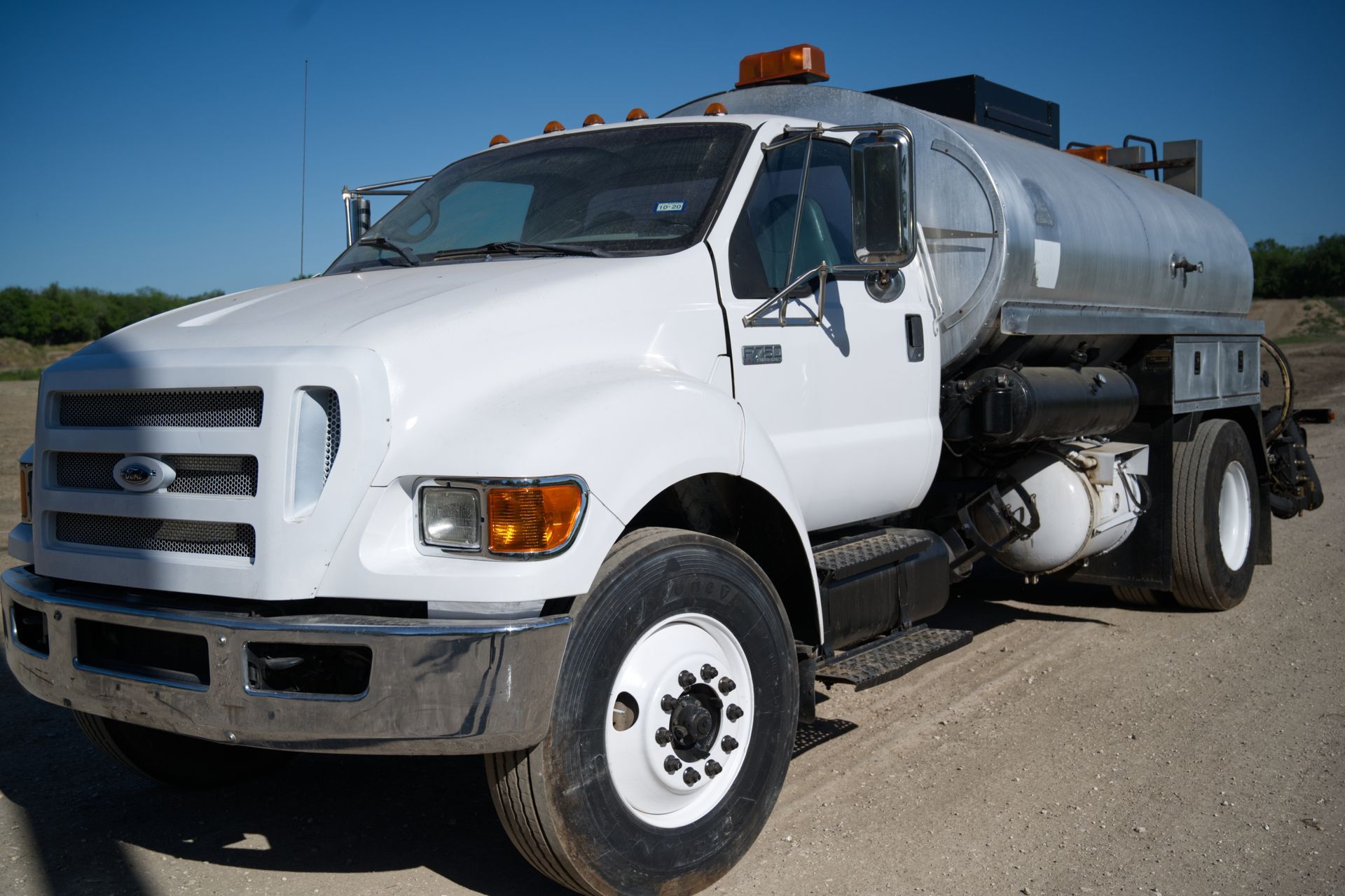 A white tanker truck is parked on a dirt road.