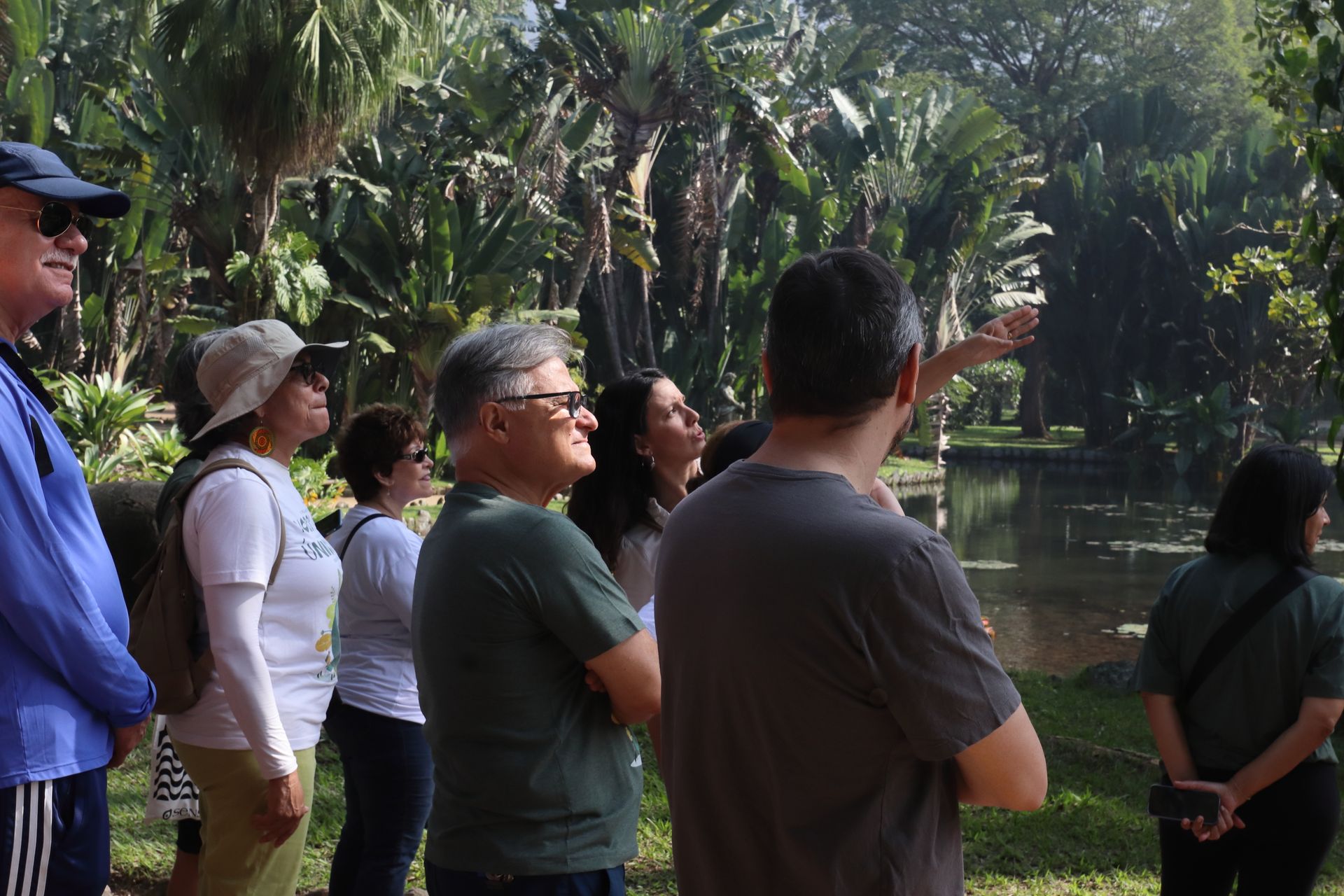 Um grupo de pessoas olha para um corpo d'água em um parque verdejante. Uma pessoa aponta para cima.
